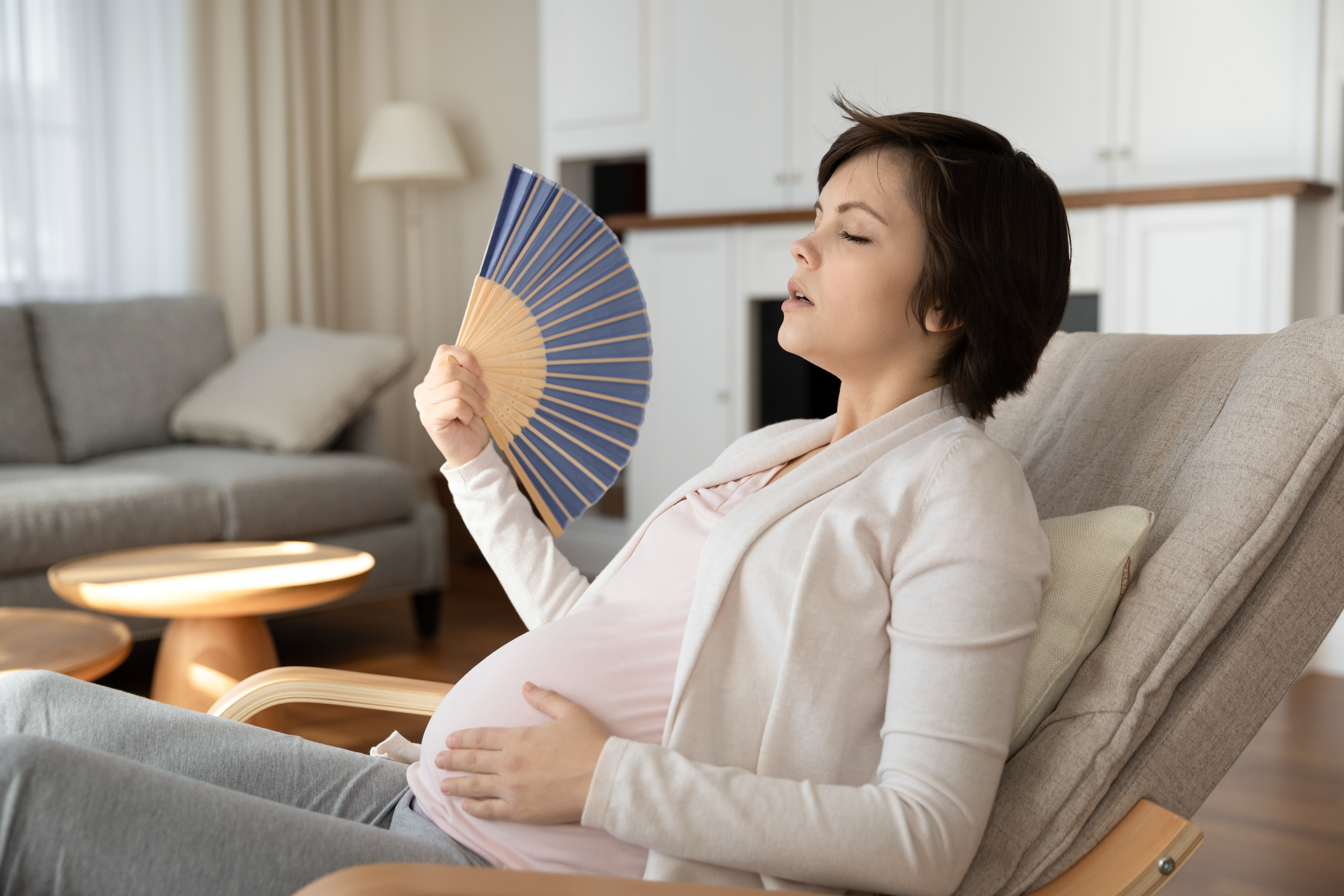 Pregnant woman sitting and fanning herself with eyes closed